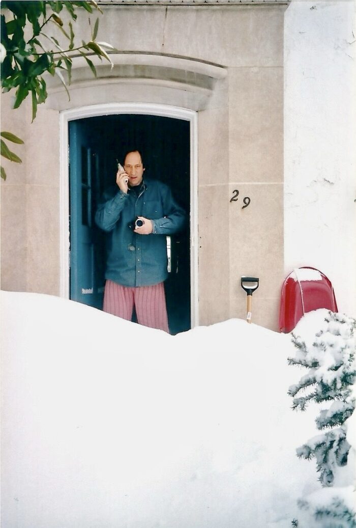 Marc Chavannes in een deurpost van een buitendeur in Washington DC, voor een sneeuwbank. Hij heeft een camera in de ene hand en een telefoon in zijn andere.